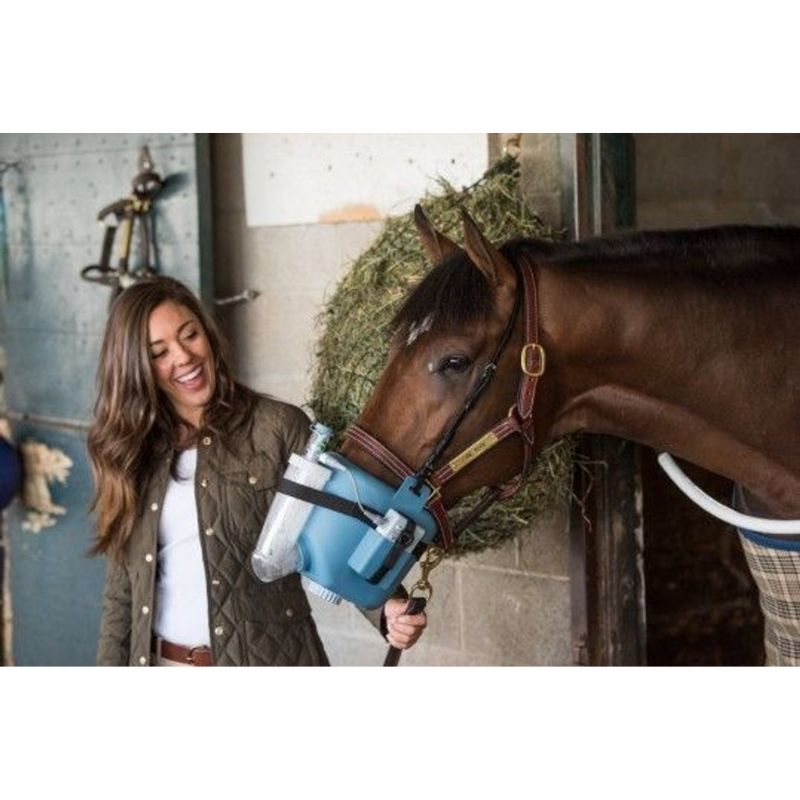 Woman holding an Equine nebulizer device next to a horse in a stable.