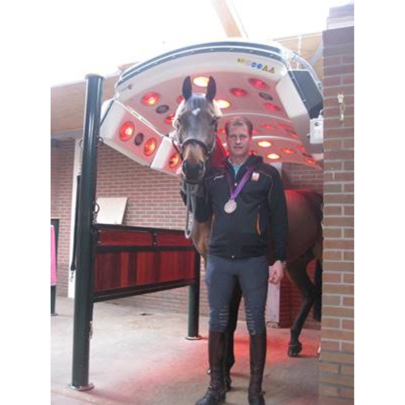 Man standing next to a horse in front of a red light therapy machine.