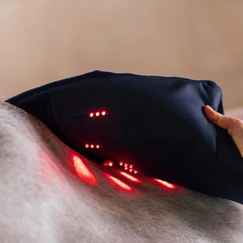 Black massage pillow with red lights on a person's back against a beige wall.